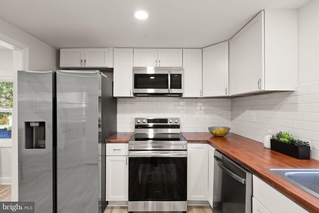 kitchen featuring white cabinets, butcher block countertops, stainless steel appliances, and decorative backsplash