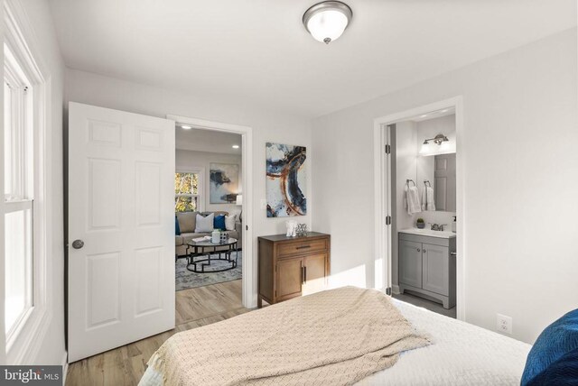 bedroom with ensuite bathroom, light wood-type flooring, and a sink