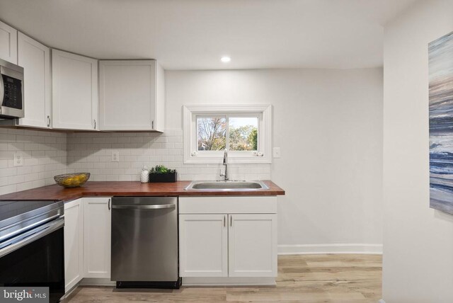 kitchen with stainless steel appliances, butcher block countertops, a sink, and white cabinets