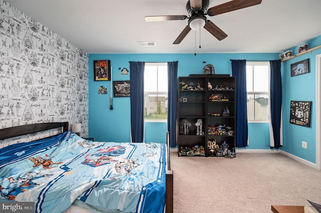 carpeted bedroom featuring an accent wall, multiple windows, and a ceiling fan