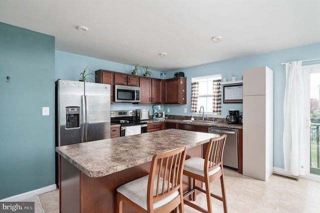 kitchen featuring appliances with stainless steel finishes, a sink, a breakfast bar area, dark brown cabinetry, and baseboards