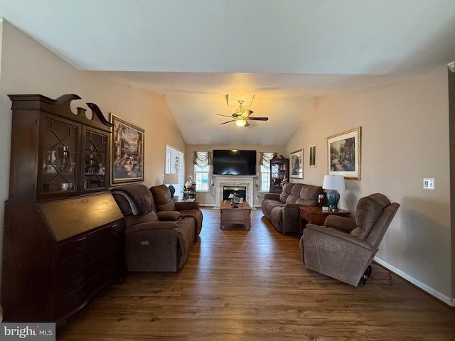 living area featuring wood finished floors, lofted ceiling, a ceiling fan, a fireplace, and baseboards