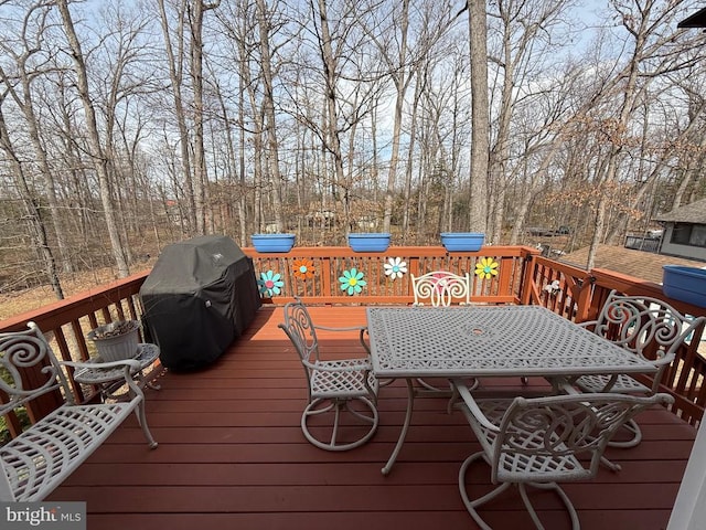 wooden terrace featuring outdoor dining area, area for grilling, and view of scattered trees