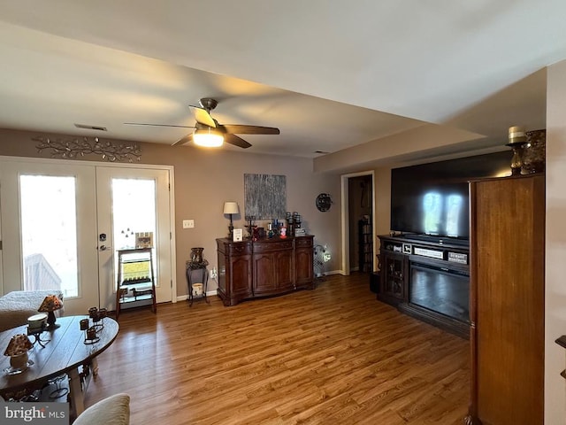 living area featuring french doors, wood finished floors, ceiling fan, and baseboards