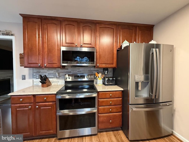 kitchen with appliances with stainless steel finishes, tasteful backsplash, light wood finished floors, and light stone counters
