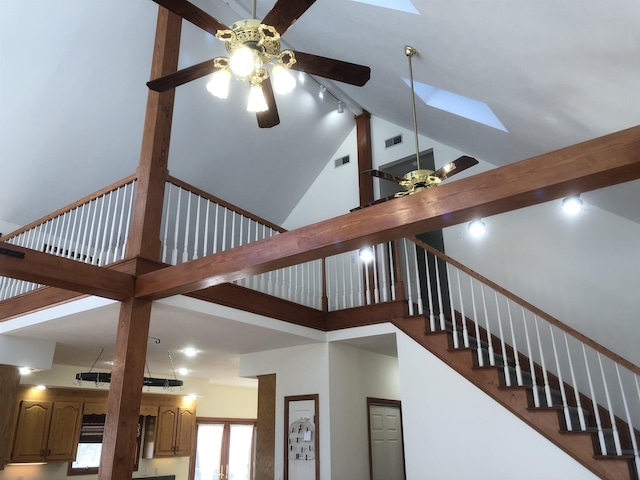 stairs with a skylight, high vaulted ceiling, track lighting, ceiling fan, and beam ceiling