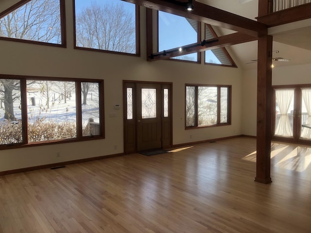 unfurnished living room featuring high vaulted ceiling, beamed ceiling, and light wood-type flooring