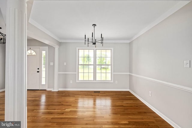  - unfurnished dining area featuring a chandelier, wood finished floors, baseboards, decorative columns, and crown molding