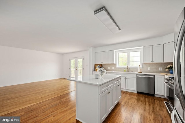  - kitchen featuring appliances with stainless steel finishes, decorative backsplash, light countertops, a kitchen island, and wood finished floors
