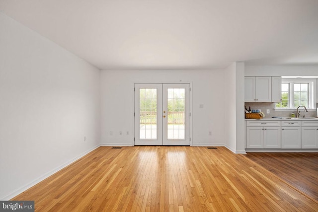  - unfurnished living room featuring light wood-style flooring, baseboards, and french doors