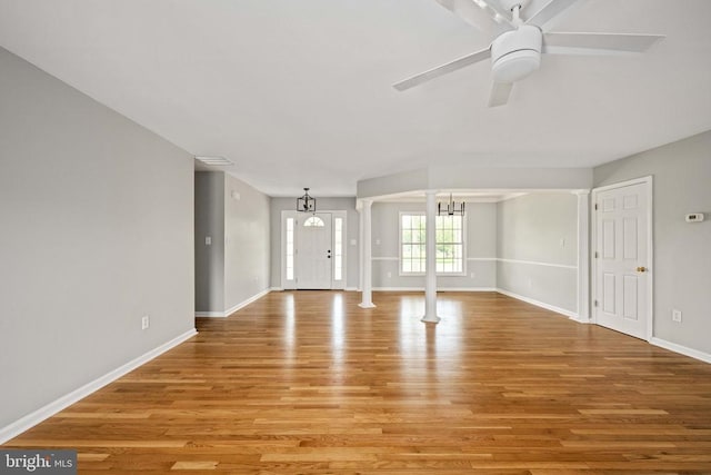  - unfurnished living room with light wood-type flooring, baseboards, a chandelier, ceiling fan, and decorative columns