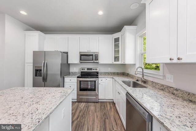 kitchen with appliances with stainless steel finishes, a sink, white cabinets, light stone countertops, and dark wood finished floors
