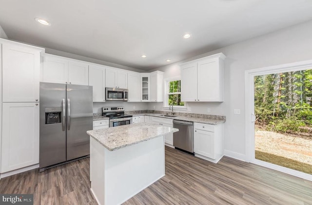 kitchen featuring stainless steel appliances, a sink, white cabinetry, wood finished floors, and light stone counters
