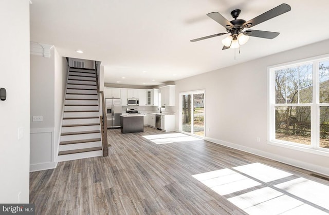 unfurnished living room with plenty of natural light, light wood-style flooring, stairway, a ceiling fan, and recessed lighting