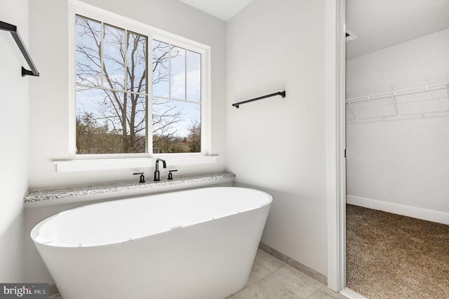 bathroom with a freestanding bath, a spacious closet, and baseboards