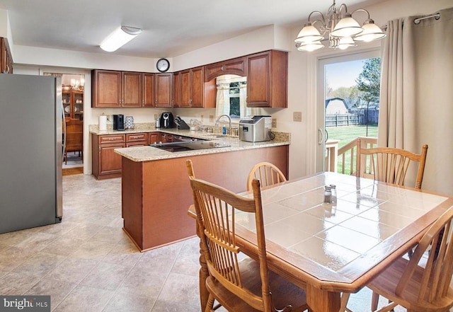 11911 Smoketree Blvd, Fredericksburg, VA 22407 - kitchen featuring a sink, a peninsula, brown cabinets, freestanding refrigerator, and an inviting chandelier