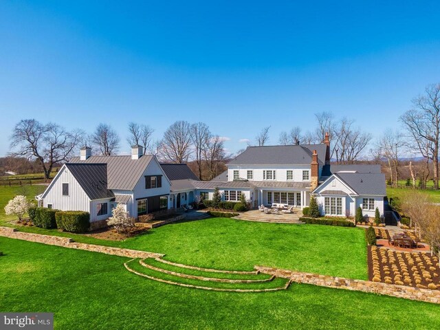 rear view of house with a chimney, metal roof, a standing seam roof, and a lawn