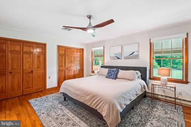  - bedroom with multiple closets, wood finished floors, a baseboard radiator, and a ceiling fan