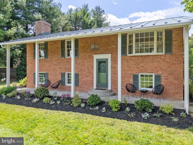 - bi-level home featuring a front yard, a chimney, a patio, and a standing seam roof