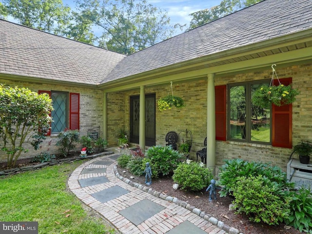  - doorway to property featuring brick siding and roof with shingles