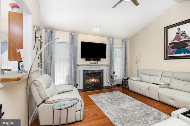 living area featuring lofted ceiling, ceiling fan, wood finished floors, and a fireplace with flush hearth
