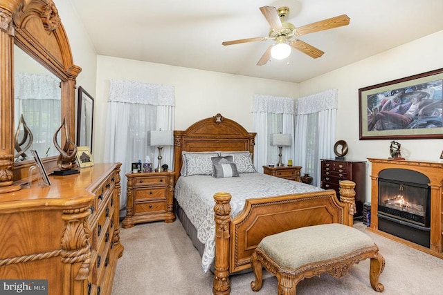 bedroom with light carpet, a glass covered fireplace, and ceiling fan