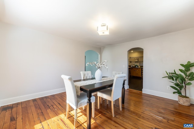 dining room featuring wood-type flooring, baseboards, and arched walkways