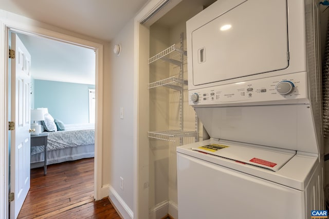 washroom with dark wood finished floors, laundry area, stacked washer / dryer, and baseboards