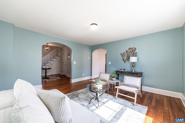 living room featuring arched walkways, stairs, baseboards, and wood finished floors