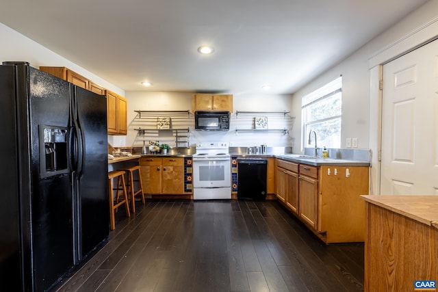 kitchen with a sink, brown cabinetry, stainless steel counters, dark wood-style flooring, and black appliances