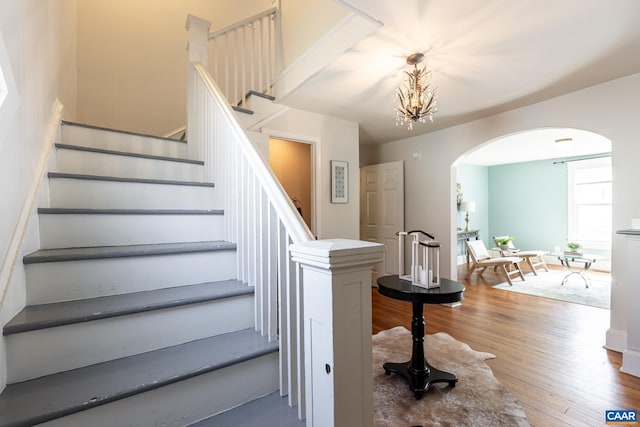 staircase featuring wood finished floors, baseboards, and arched walkways