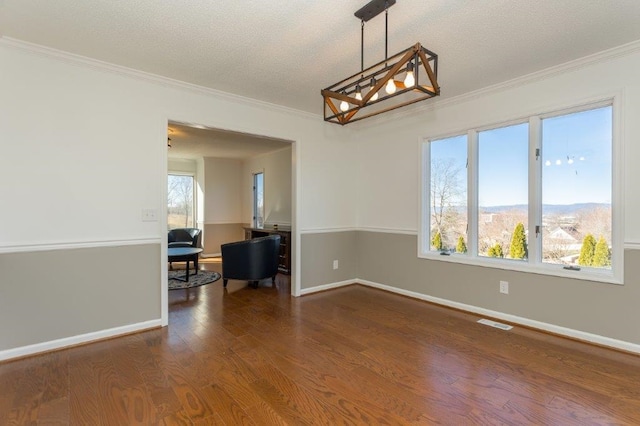 empty room featuring crown molding, a chandelier, a textured ceiling, a mountain view, and hardwood / wood-style flooring