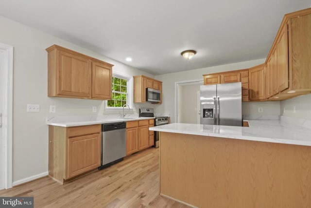 kitchen featuring stainless steel appliances, a sink, light wood-style flooring, and a peninsula