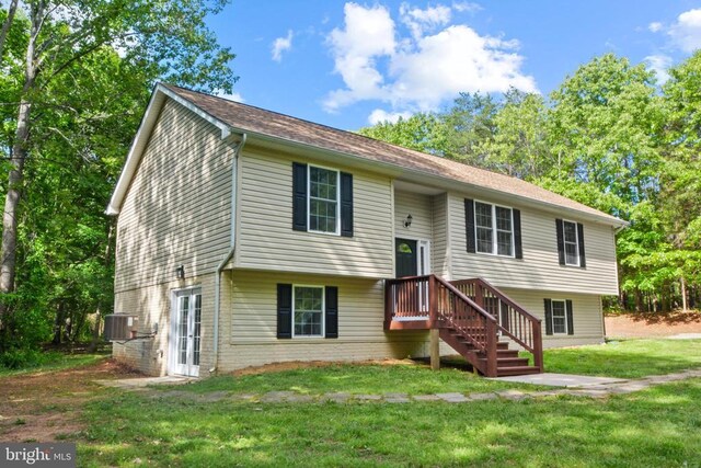 raised ranch with central air condition unit, a front yard, and brick siding