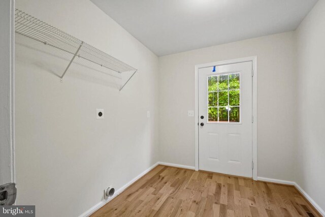 clothes washing area featuring electric dryer hookup, light wood-type flooring, and baseboards