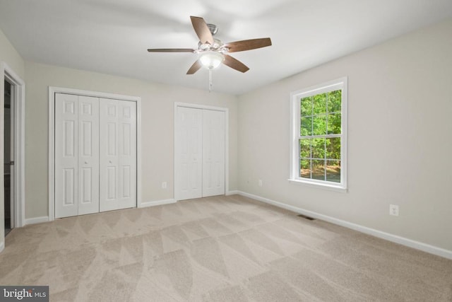 unfurnished bedroom featuring multiple closets, baseboards, and light colored carpet