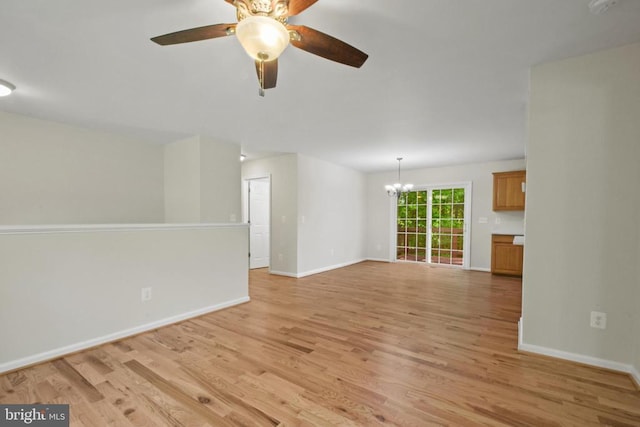 empty room with a chandelier, light wood finished floors, a ceiling fan, and baseboards