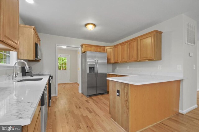 kitchen featuring appliances with stainless steel finishes, a sink, light wood-type flooring, a peninsula, and baseboards