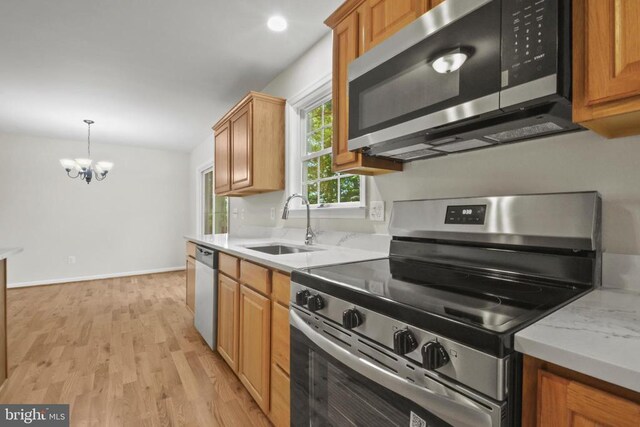 kitchen featuring appliances with stainless steel finishes, a sink, a chandelier, light wood-style flooring, and brown cabinetry