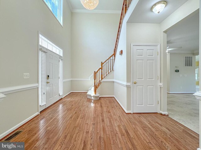foyer featuring stairs, light wood-type flooring, ornamental molding, and baseboards