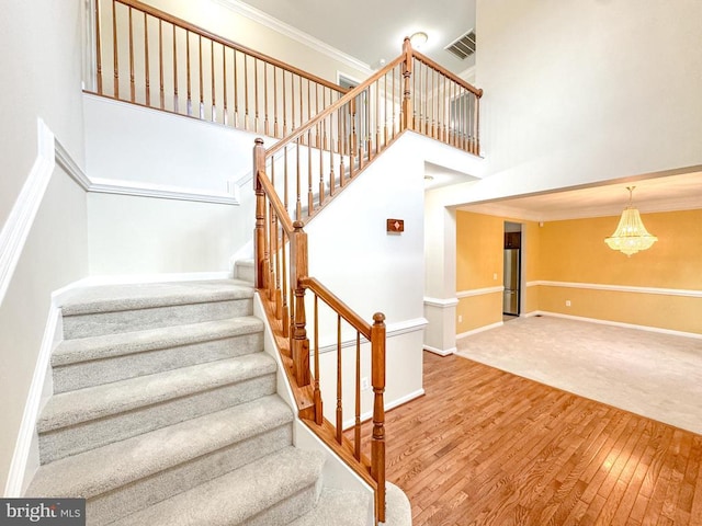 stairs with a high ceiling, wood finished floors, baseboards, a chandelier, and crown molding