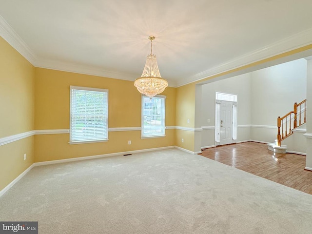 carpeted empty room with a chandelier, ornamental molding, baseboards, and stairway