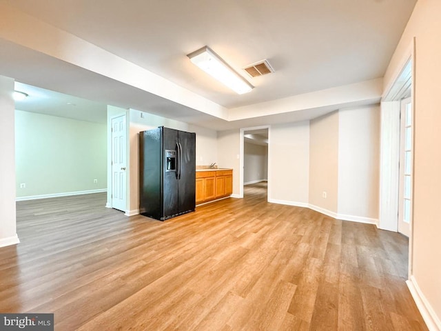 below grade area with black refrigerator with ice dispenser, light wood finished floors, and baseboards