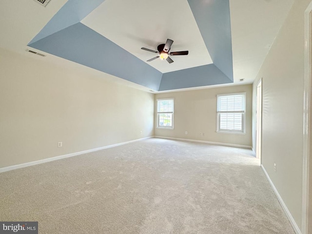 unfurnished room featuring a tray ceiling, ceiling fan, carpet, and baseboards