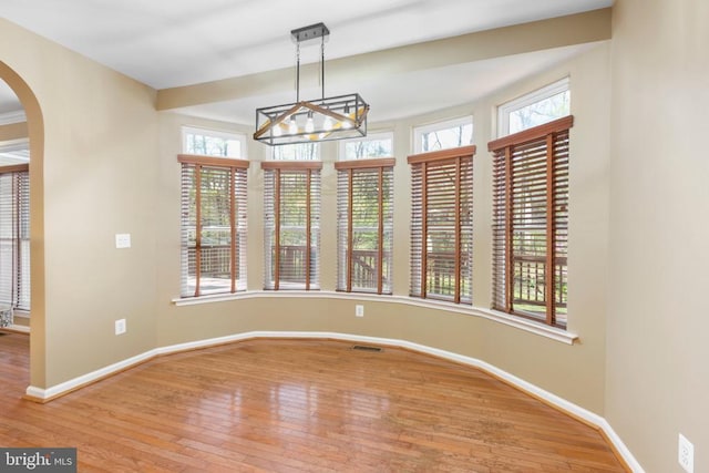 unfurnished dining area with hardwood / wood-style floors, plenty of natural light, a chandelier, and baseboards