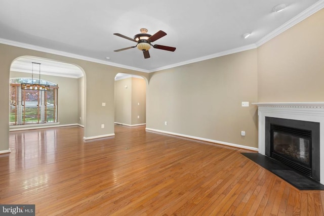 unfurnished living room featuring light wood-style flooring, ceiling fan, crown molding, a glass covered fireplace, and arched walkways