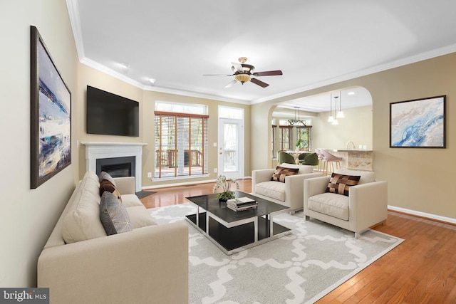 living area featuring arched walkways, wood finished floors, crown molding, baseboards, and ceiling fan