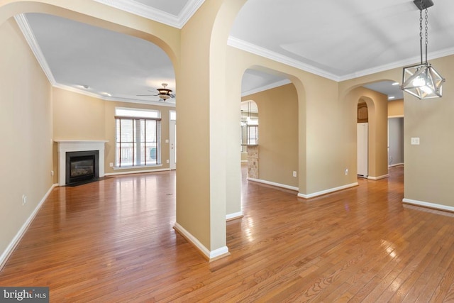 unfurnished living room with a ceiling fan, light wood-style flooring, a fireplace with flush hearth, crown molding, and baseboards
