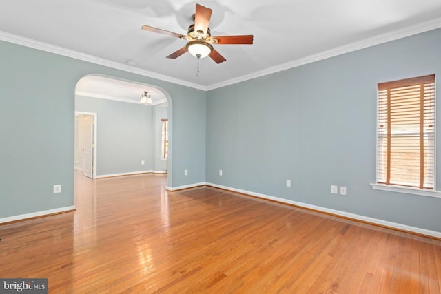 spare room featuring ceiling fan, arched walkways, wood finished floors, baseboards, and crown molding