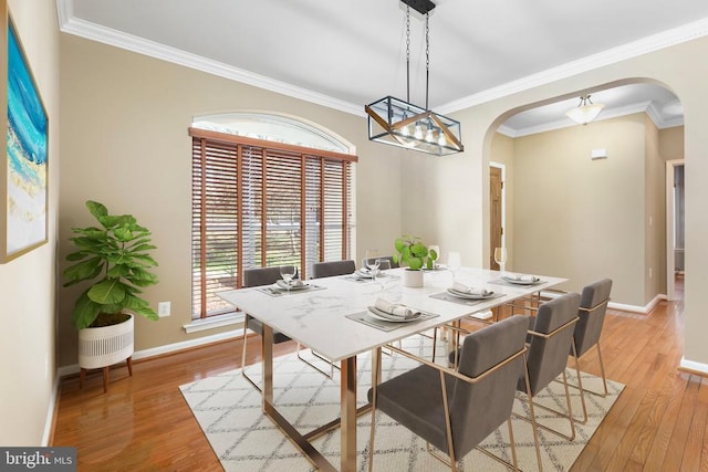 dining room with arched walkways, light wood-style flooring, baseboards, and ornamental molding